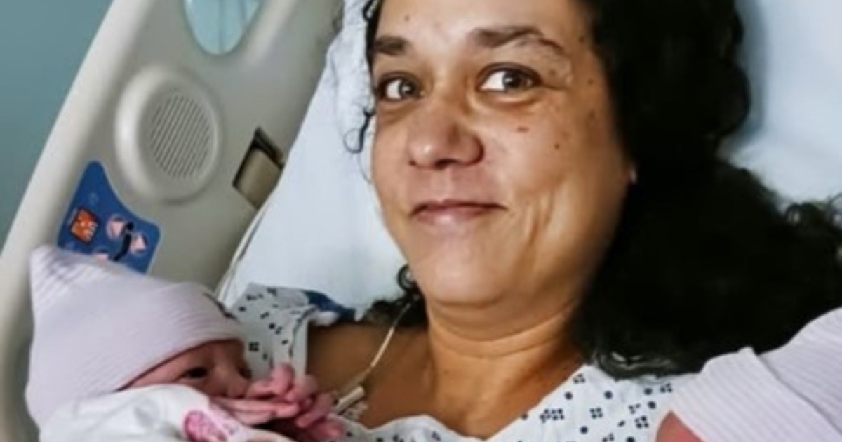 Femme d'&acirc;ge m&ucirc;r tenant des v&ecirc;tements de b&eacute;b&eacute;, l'air &agrave; la fois &eacute;merveill&eacute;e et pensive.