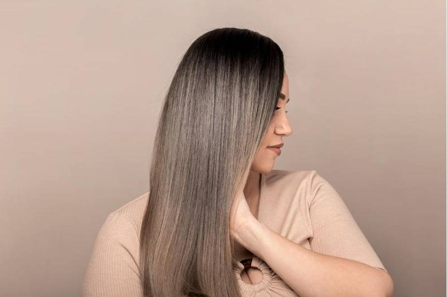 Femme aux cheveux lisses et brillants, tenant une feuille verte